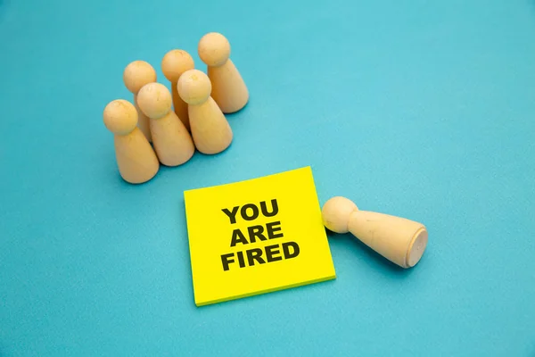 Drewniane pionki w pobliżu żółtej, lepkiej kartki z wiadomością "Jesteś zwolniony". Koncepcja bezrobocia — Zdjęcie stockowe