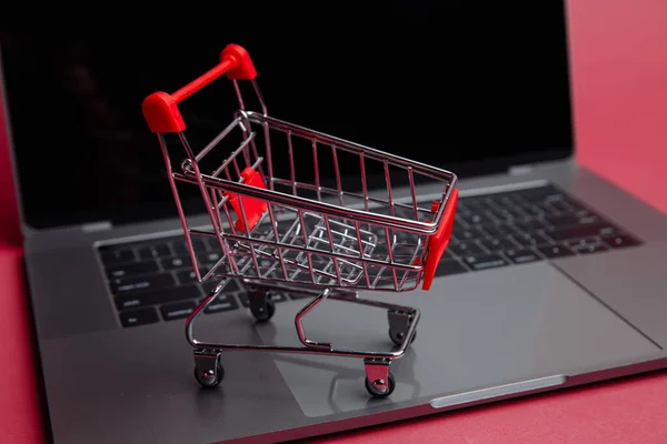 Online einkaufen. Laptop und Körbchen auf rosa Hintergrund. — Stockfoto