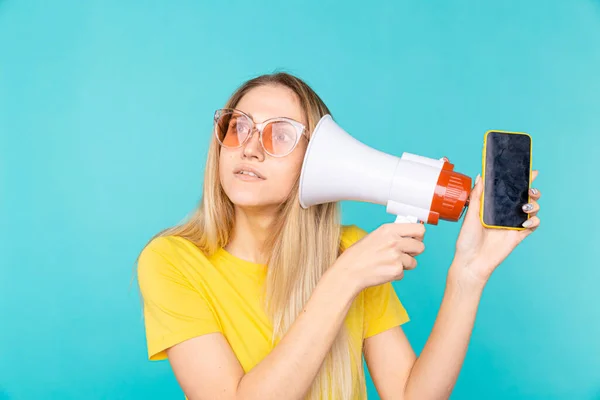 Jonge vrouw met een megafoon of luidspreker. Meisje toont mobiele telefoon scherm, smartphone in de hand — Stockfoto