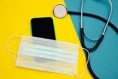 Renkli arkaplan üzerine metin için stetoskop, yüz maskesi ve cep telefonu