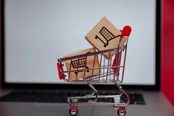 Concepto de compras online. Portátil con mini carro de mercado y cajas — Foto de Stock