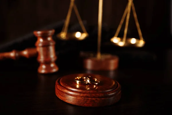 Los anillos de boda en el soporte del árbol, el martillo del juez sobre el fondo de madera. Procedimientos de divorcio —  Fotos de Stock