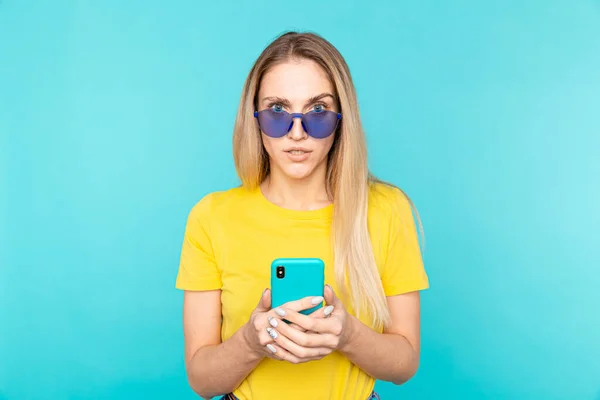 안경을 쓴 젊은 여자가 푸른 색다른 배경 위에서 서 카메라를 바라본다. 젊음 과 기술 — 스톡 사진