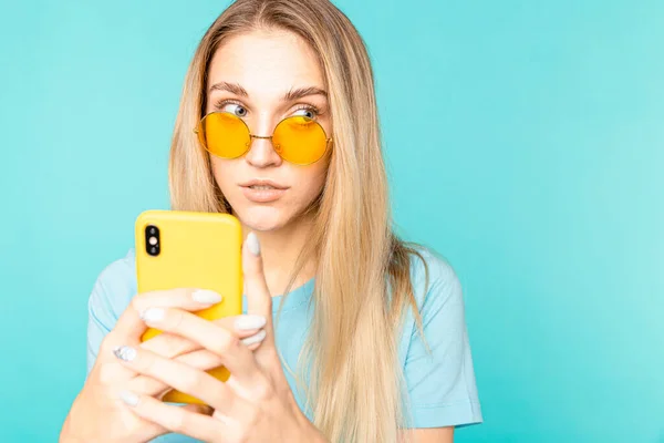 Imagen de una chica con una camiseta azul lee cuidadosamente un mensaje en su teléfono inteligente — Foto de Stock