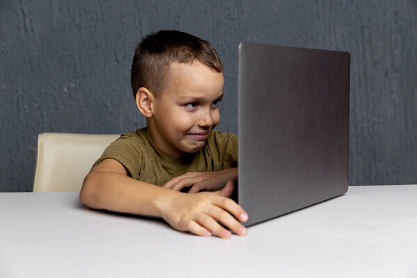 Upset boy sitting and studying on the computer online at quarantine time.