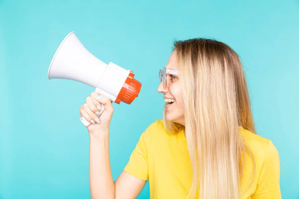 Jovem mulher em camiseta amarela sobre a parede azul gritando através de um megafone e sorrindo — Fotografia de Stock