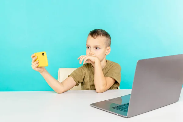 Menino feliz na educação à distância falando alguém telefone e usando o computador para estudar . — Fotografia de Stock