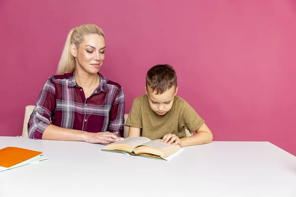 Die attraktive junge Frau und ihr kleiner Sohn sitzen am Tisch und machen gemeinsam Hausaufgaben. Mutter hilft Sohn bei Schulklassen — Stockfoto