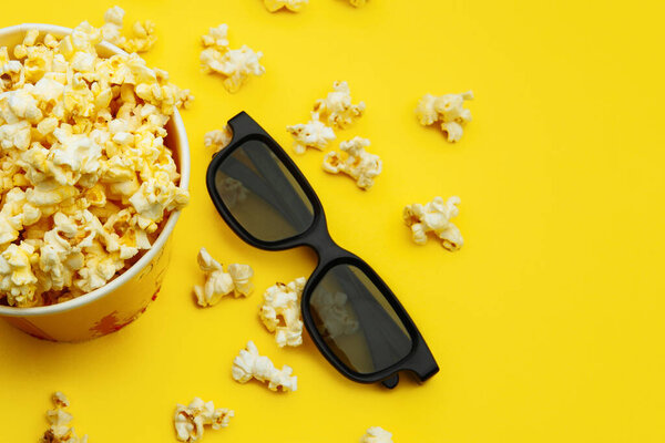Popcorn in a bowl and 3d glasses on yellow background, top view