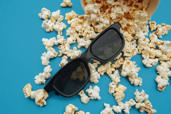 Popcorn versato fuori dalla ciotola. Occhiali per la visione del film sono su uno sfondo blu — Foto Stock
