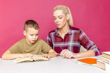 Anne, oğluna pembe arka planda ödevlerinde yardım ediyor. Uzak eğitim