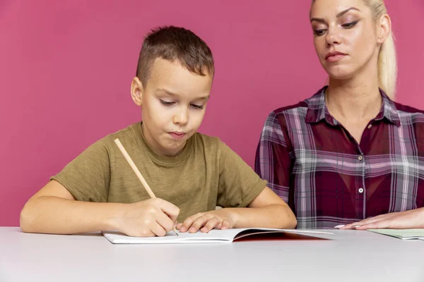 隔離概念で一緒に宿題をする。本と勉強で机に座ってる子供の母親. — ストック写真