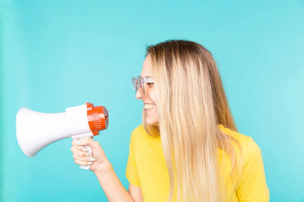 Junge Frau mit Sonnenbrille über blauer Wand brüllt durch Megafon und lächelt — Stockfoto