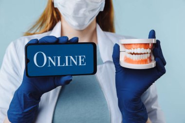 Diş kliniğinde poz veren güzel bir kadın dişçinin portresi. Elinde yeşil ekranlı akıllı telefon var ve kameraya mobil uygulama veya web sitesi sunuyor.