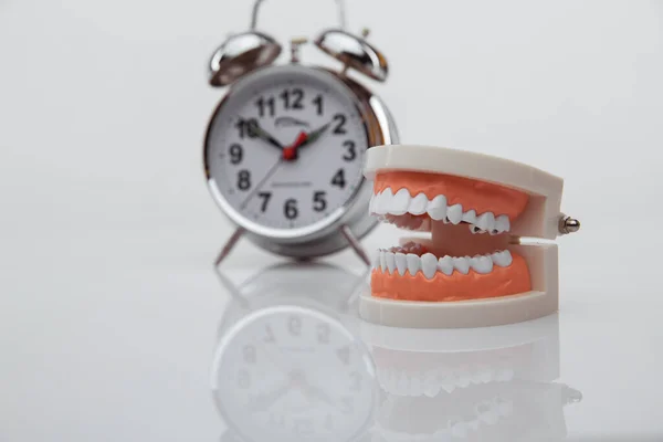 青い背景に目覚まし時計付きの白い紙の歯。歯の健康への時間。歯医者の日の概念。フラットレイアウト、トップビュー、テキストのコピースペース. — ストック写真