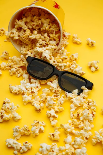 Popcorn versato fuori dalla ciotola. Occhiali per la visione del film sono su uno sfondo giallo — Foto Stock