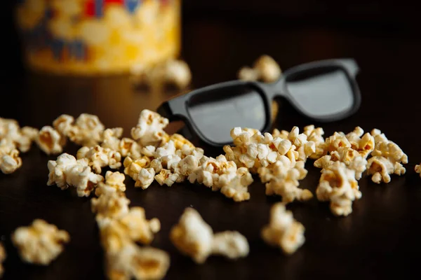 Popcorn versato fuori dalla ciotola. I bicchieri 3d sono su uno sfondo di legno. Concetto di Entetainement . — Foto Stock