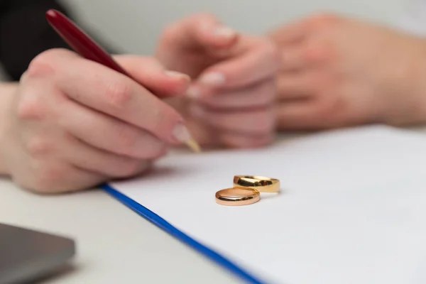 Развод в процессе. Женщина и мужчина подписывают документ. Обручальные кольца на столе . — стоковое фото