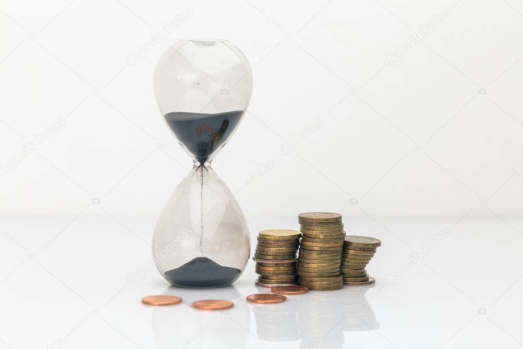 Hourglass with a lot of coins at the desk isolated over the white background.