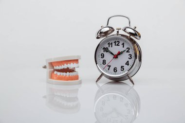 Mavi arka planda alarm saati olan beyaz kağıt diş. Diş sağlığı zamanı. Dişçi günü konsepti. Düz konum, üst görünüm, metin için boşluk kopyala.