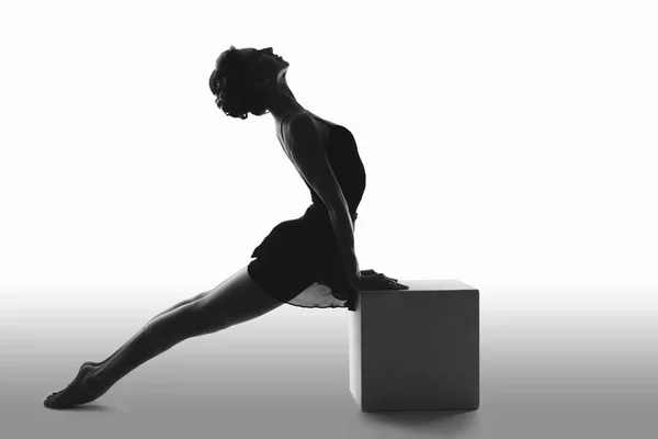 Beautiful ballet dancer posing in the Studio performing the deflection in the back and leaning on a big cube silhouette — Stock Photo, Image