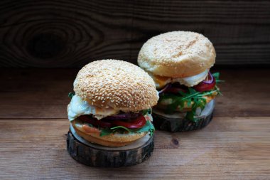 İki hamburger ekmeği susam, roka, yumurta ile karanlık bir arka plan üzerinde doğal ahşap stand pirzola yatıyor