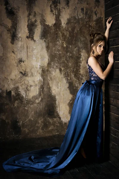 Mooie jonge brunette meisje poseren op donkere achtergrond in blauwe lange jurk en feestelijke avond deel — Stockfoto