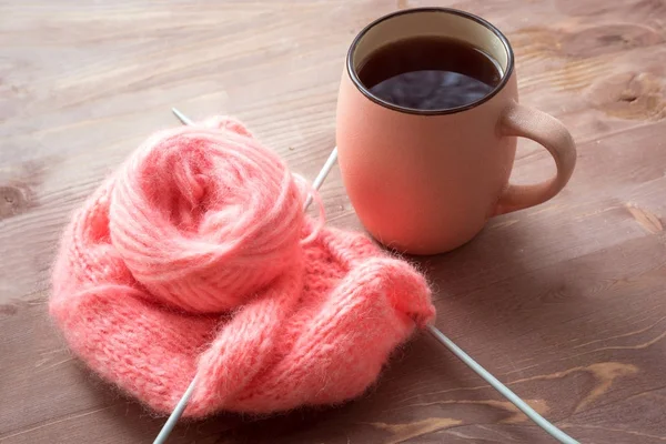 Rosa Tasse heißen Tee und Stricken in rosa Wolle mit Nadeln auf hölzernem Hintergrund — Stockfoto