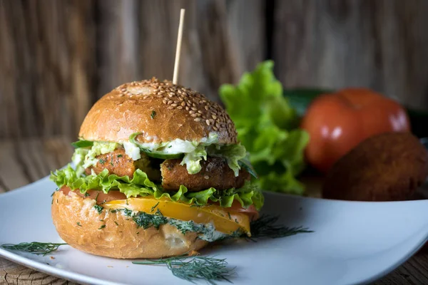 Veggie Burger en un bollo de semillas de sésamo con lechuga jugosa y tomate sobre fondo de madera —  Fotos de Stock