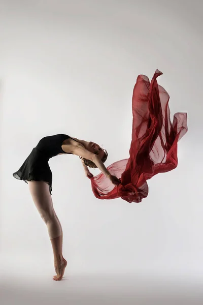 Dançarina de balé graciosa dançando em um fundo leve com um pano vermelho fluido e leve — Fotografia de Stock