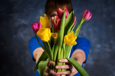 mavi elbiseli kız onun kollarında bir buket sarı-kırmızı laleler, yüzünü kaplayan tutar