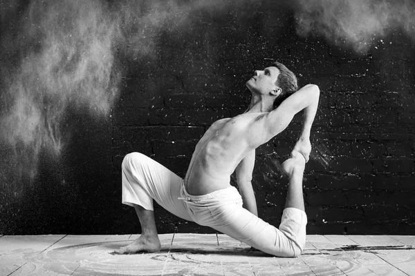 Um homem fazendo ioga em uma nuvem branca de poeira em uma sala escura. O conceito de energia. Foto preto-e-branco . — Fotografia de Stock