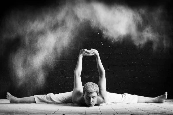 Um homem fazendo ioga em uma nuvem branca de poeira em uma sala escura. O conceito de energia. Foto preto-e-branco . — Fotografia de Stock