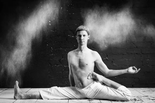 Um homem fazendo ioga em uma nuvem branca de poeira em uma sala escura. O conceito de energia. Foto em preto e branco. Hatha ioga. Hanumanasana a pose do rei macaco — Fotografia de Stock