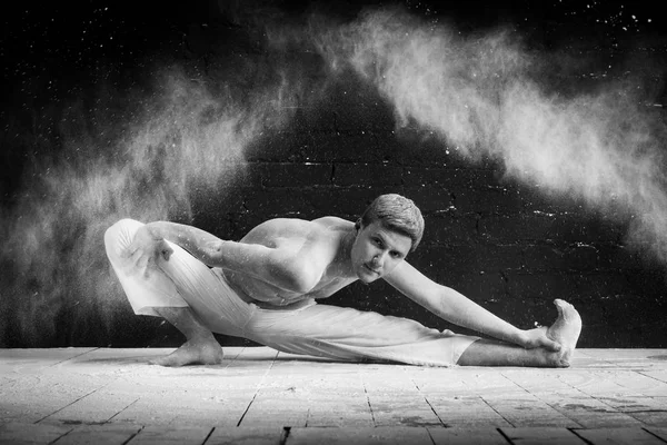 Um homem fazendo ioga em uma nuvem branca de poeira em uma sala escura. O conceito de energia. Foto preto-e-branco . — Fotografia de Stock