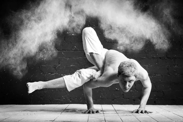 Um homem fazendo ioga em uma nuvem branca de poeira em uma sala escura. O conceito de energia. Foto em preto e branco. Hatha ioga. Parshva, Bhuj Dandasana - pose do Hummingbird — Fotografia de Stock