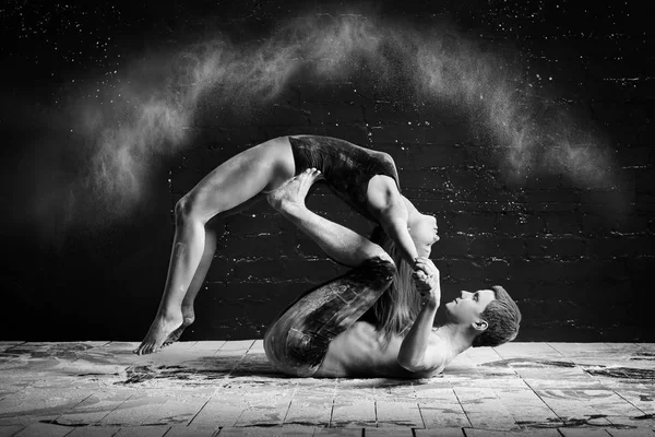 Homem e mulher fazendo ioga fumegante em uma nuvem de poeira em um fundo preto. akroyoga — Fotografia de Stock