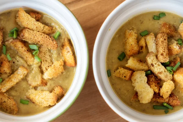 two soup cups with vegetable soup-puree with croutons and green onions on a wooden Board