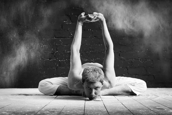 Um homem fazendo ioga em uma nuvem branca de poeira em uma sala escura. O conceito de energia. Pada-Prasar-pashchimottanasana (pose para esticar a superfície posterior do corpo com as pernas afastadas ) — Fotografia de Stock