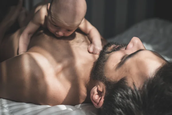 Newborn baby lying on father body in bed — Stock Photo, Image