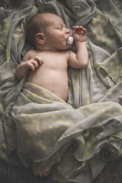 Sleeping newborn baby laying on the bed wrapped in the scarf — Stockfoto