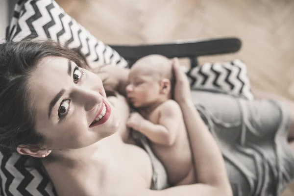 Morbida foto sorridente giovane madre che allatta il seno il suo bambino a casa . — Foto Stock