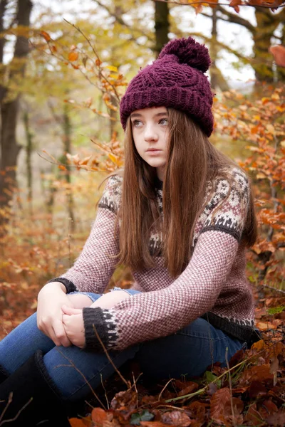 Pretty young girl sitting on dried leaves in a forrest — Stock Photo, Image