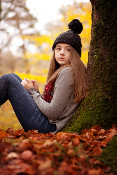 Hübsches junges Mädchen sitzt im Herbst gegen einen Baum — Stockfoto