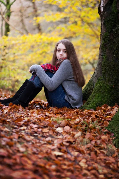 Hezká mladá dívka sedí na sušené listy v lese — Stock fotografie
