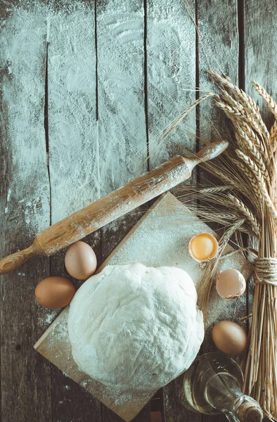 stock image Kneaded dough, ears of wheat,rolling pin, eggs and a bottle of oil on the old rustic table