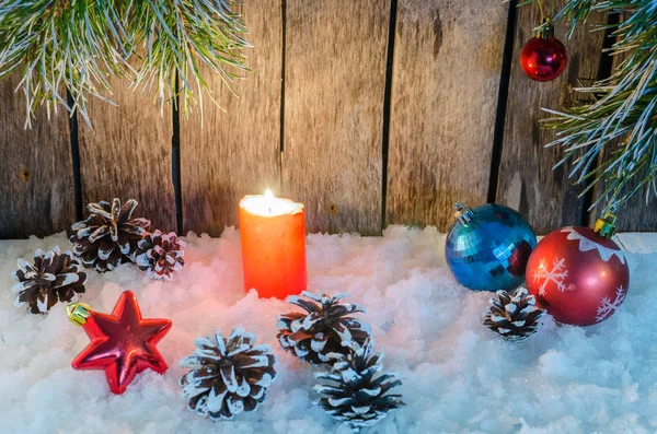 Christmas ornament, red candle and toys in the snow on a wooden background and tree branches — Stock Photo, Image