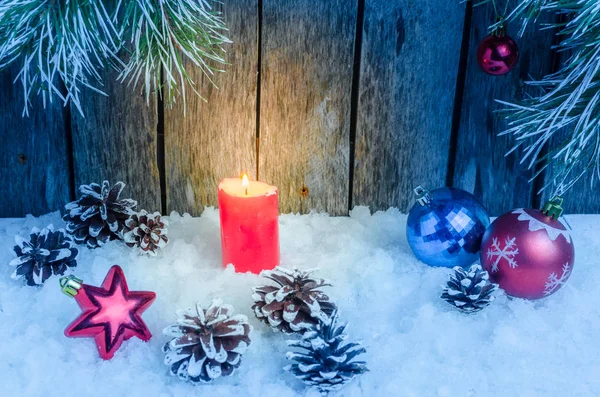 クリスマスの飾り、赤いろうそくと木製の背景と木の枝の雪の中のおもちゃ — ストック写真