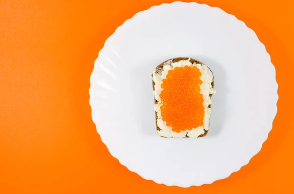 A piece of black rye bread on a white plate smeared with butter and red caviar — Stock Photo, Image
