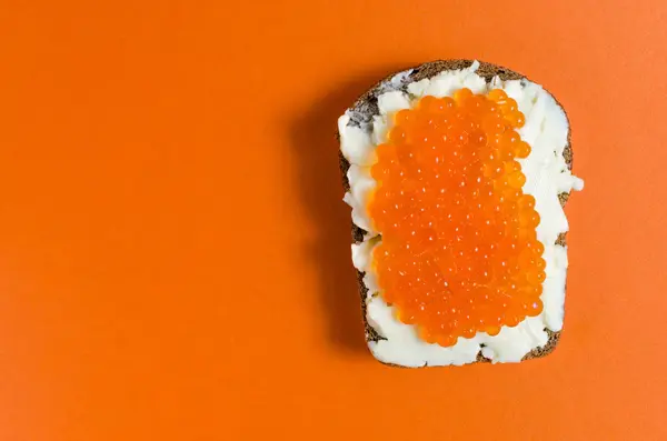 A piece of black rye bread, smeared with butter and red caviar — Stock Photo, Image